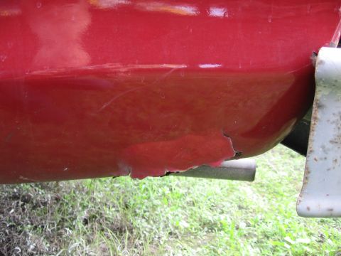 1974 Ford F-100 - The lower body panel of a red vehicle shows significant rust damage and peeling paint.