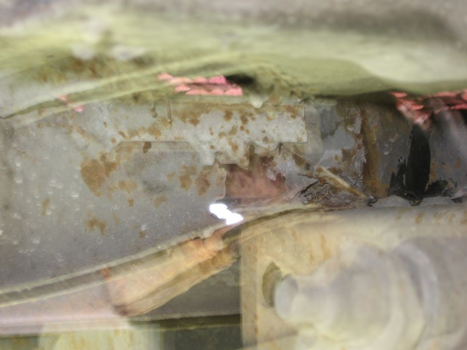 Undercarriage of a heavily rusted vehicle, showing frame damage and corrosion. A 'SUPERMOTORS' watermark is visible