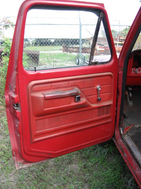 1974 Ford F-100 - Interior view of a red truck door panel, showing the armrest, window crank, and speaker grille.