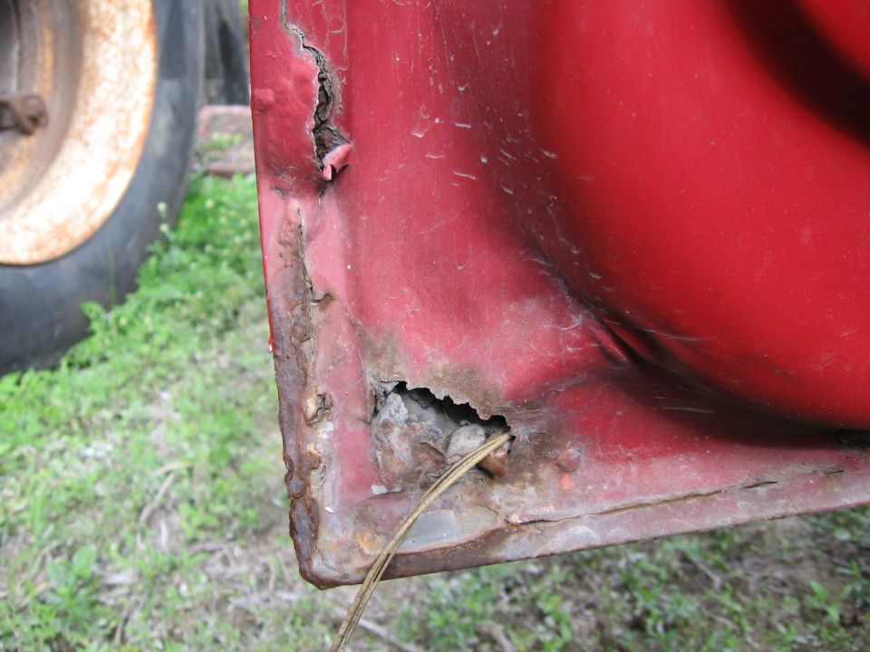 1974 Ford F-100 door corner with significant rust damage and holes. A wire protrudes from a hole