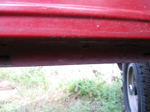 1974 Ford F-100 - A close-up view of the lower body panel of a red vehicle, showing some wear and a portion of a tire.