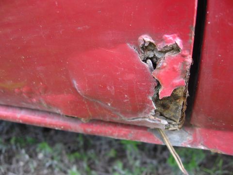 1974 Ford F-100 - Close-up of severe rust on a red truck door, indicating poor condition.