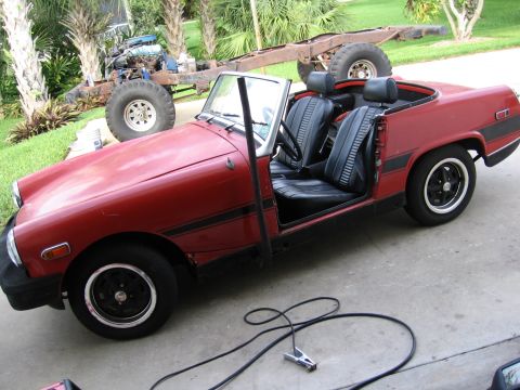 1974 Ford F-100 - A red convertible sports car sits in a driveway next to a separate vehicle chassis with an engine.