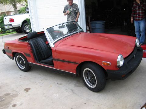 1974 Ford F-100 - Red convertible sports car parked in front of a garage, with a white pickup truck in the background.