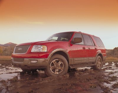 2003 Ford Expedition - A red 2003 Ford Expedition navigates through a muddy terrain undergrowth during a sunset.