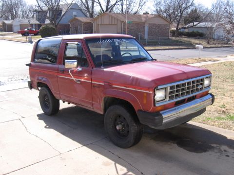 1984 Ford Bronco II - This red Ford Bronco II is parked on a concrete driveway in front of suburban houses.