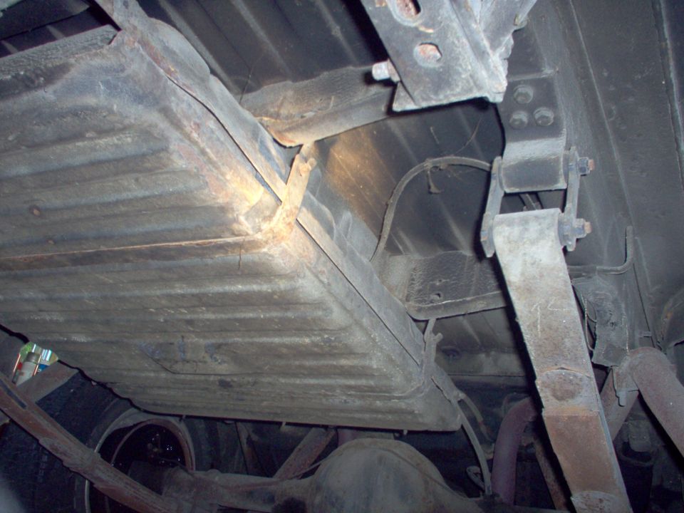 Underside view of corrugated fuel tank, strap, frame rail and leaf spring shackle