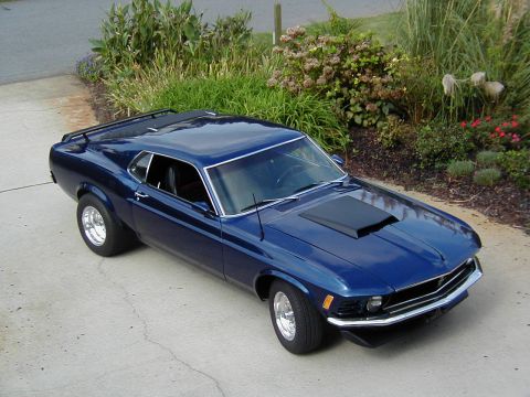 1970 Ford Mustang - A blue 1970 Ford Mustang coupe is parked on a concrete driveway, with landscaping visible behind it.