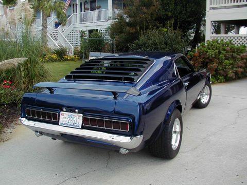 1970 Ford Mustang - Rear view of a dark blue coupe with distinctive louvers and a spoiler, parked in front of a house.