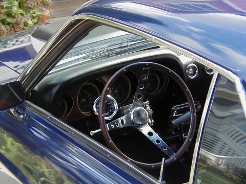 1970 Ford Mustang - The interior of a classic car features a wood-rimmed steering wheel and a dashboard with multiple gauges.