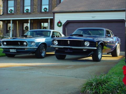 1970 Ford Mustang - Two classic Ford Mustangs, a blue 1969 model and a dark blue 1969 model, are parked in front of a residential garage.