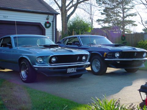 1970 Ford Mustang - Two blue Ford Mustangs are parked in a driveway, with one in the foreground and another behind it.