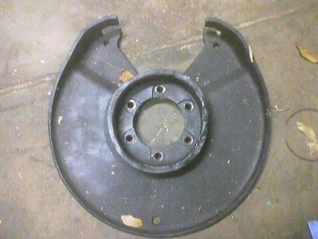 black metal dust shield with six bolt holes around a central opening