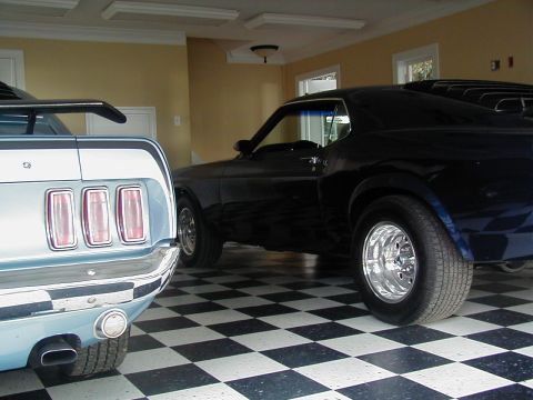 1970 Ford Mustang - Two classic Ford Mustangs, a light blue and a black one, parked side-by-side in a garage.
