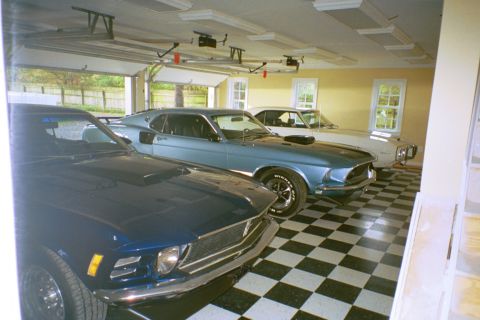1970 Ford Mustang - Three classic cars, including a blue 1969 Ford Mustang Mach 1, are parked in a garage with a checkered floor.