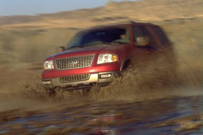 2003 Ford Expedition - A red 2003 Ford Expedition navigates a muddy terrain, kicking up water and dirt.