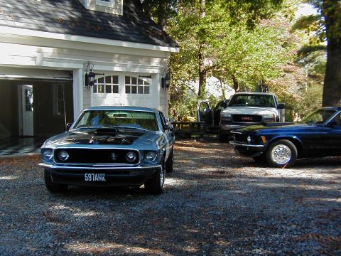 1970 Ford Mustang - A blue 1969 Ford Mustang is parked in front of a garage, with a GMC pickup and another Mustang behind it.