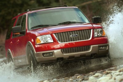 2003 Ford Expedition - A red 2003 Ford Expedition splashes through water on a rocky surface.