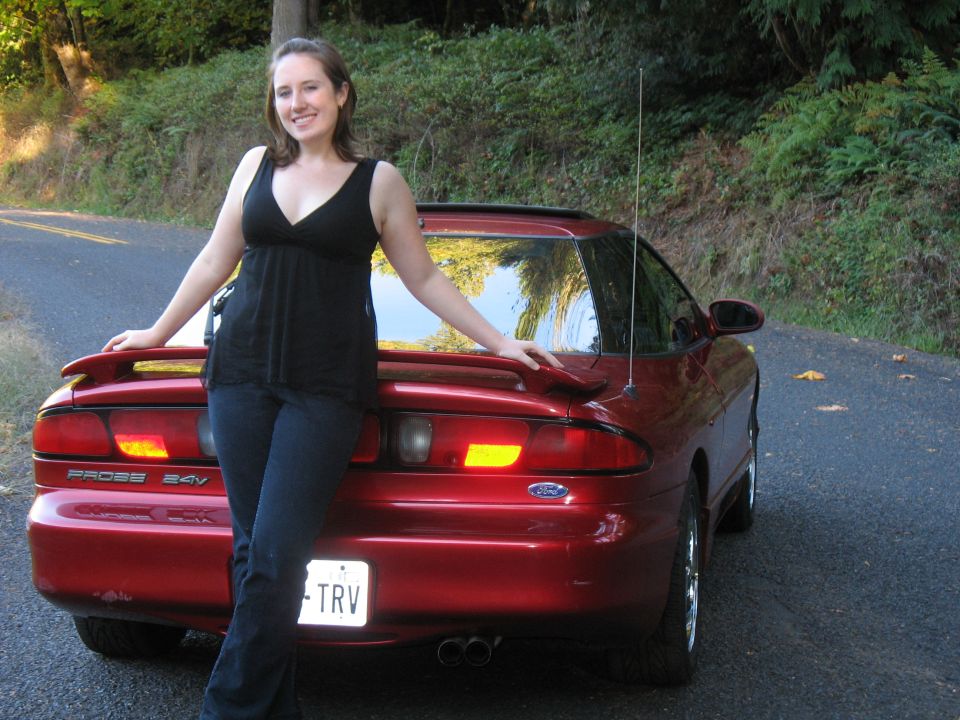 Woman leaning on a red 1997 Ford Probe. The car has a spoiler and dual exhaust pipes