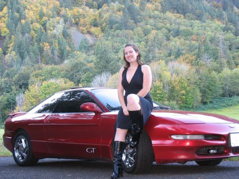 1997 Ford Probe - A woman poses on the hood of a red 1997 Ford Probe GT coupe, with a backdrop of autumn foliage.