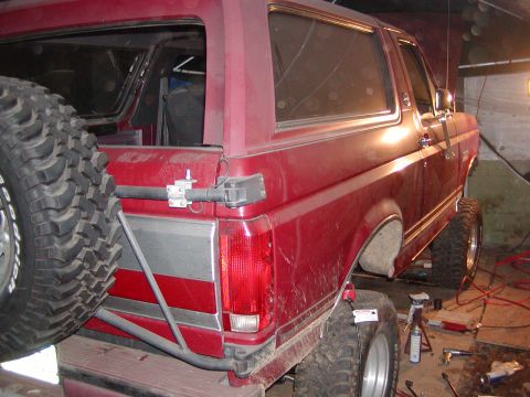 1991 Ford Bronco - The rear of a red Ford Bronco is shown with a spare tire mounted externally and a lifted suspension.