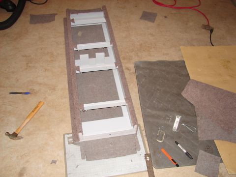 1996 Ford Bronco - A car stereo mounting bracket, partially covered in carpet, lies on the floor next to tools and other materials.