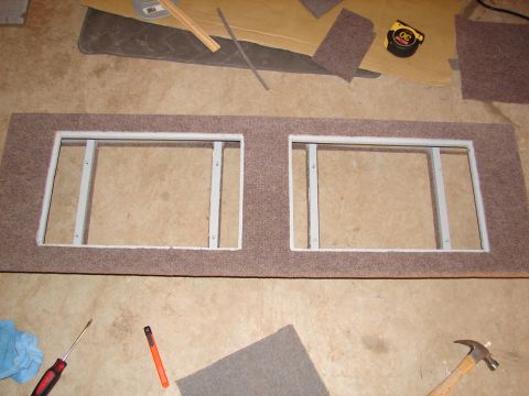 1996 Ford Bronco - A carpeted panel with two openings, likely for speakers or gauges, is on a concrete floor with tools nearby.
