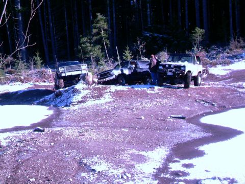1987 Ford Bronco II - Three off-road vehicles, including a 1987 Ford Bronco II, are parked in a snowy forest clearing.