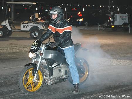1965 Ford Mustang - Motorcyclist performs a burnout, creating a cloud of smoke. Other vehicles are visible in the background.