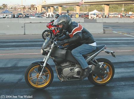 1965 Ford Mustang - Two motorcycles are racing down a drag strip with a crowd in the background.