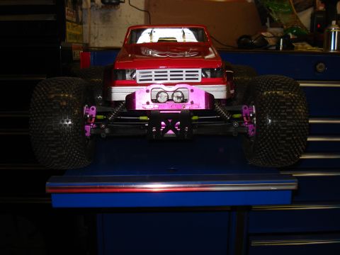1994 Ford Bronco - A red remote control monster truck sits on a blue surface, its large tires and custom pink suspension visible.