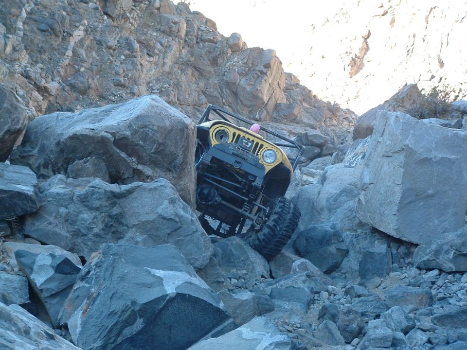 Yellow 1994 Jeep YJ navigating a steep, rocky trail with its front wheels angled up