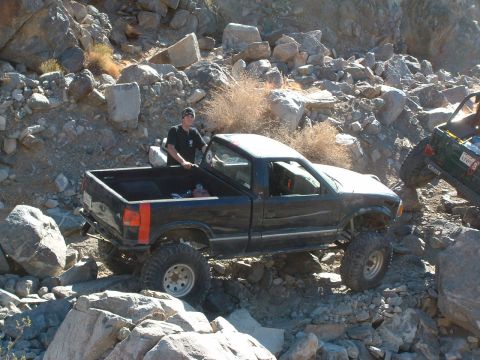 1994 Jeep YJ - A black pickup truck is driven off-road with another vehicle visible in the background.