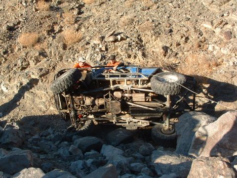 1994 Jeep YJ - An off-road vehicle has rolled onto its side amidst a rocky, desert-like landscape.