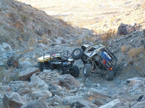 1994 Jeep YJ - Two custom off-road vehicles traverse a challenging rocky terrain on a sunny day.