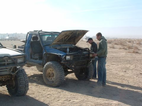 1994 Jeep YJ - Two men inspect the engine of a modified blue pickup truck in a desert landscape.