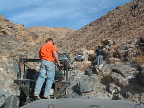 1994 Jeep YJ - Off-road vehicles traverse a challenging rocky mountain path under a clear blue sky.