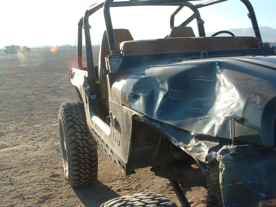 Damaged 1994 Jeep YJ with dented fender and hood, parked on dirt