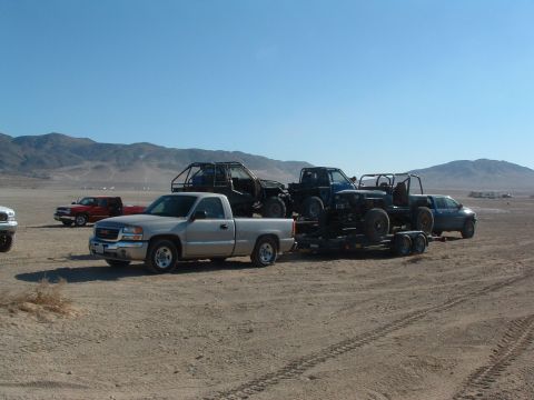 1994 Jeep YJ - Several trucks and off-road vehicles are parked in a desert landscape under a clear blue sky.