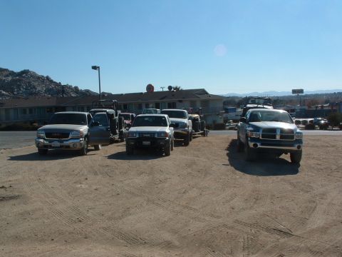 1994 Jeep YJ - Multiple pickup trucks are parked on a dirt lot under a clear blue sky.