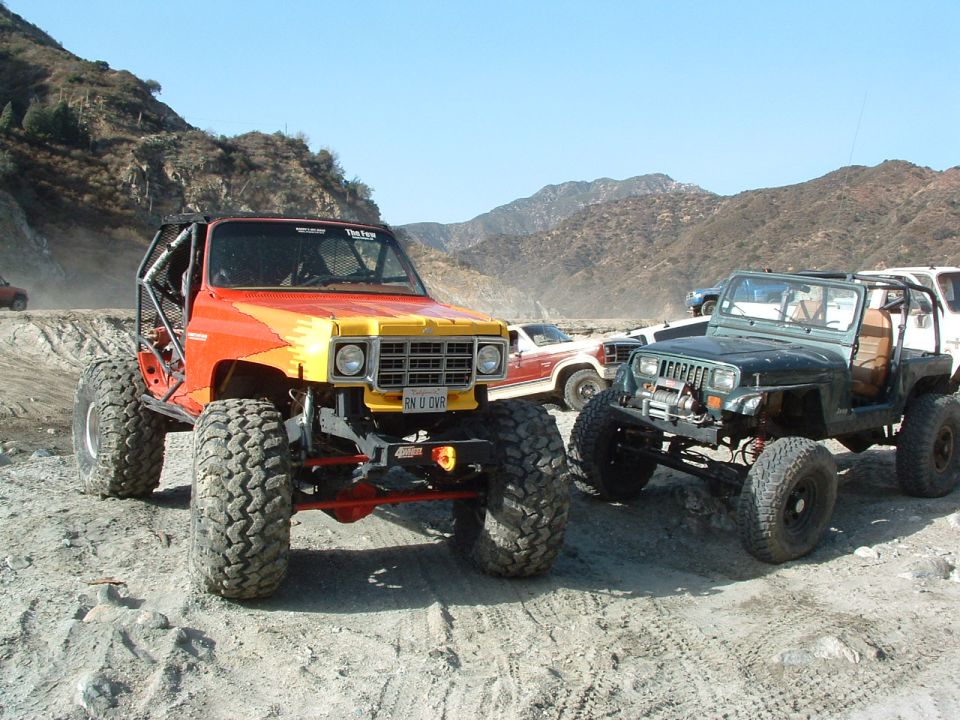 1994 Jeep YJ with custom roll cage and large tires, parked next to another modified Jeep