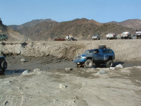 1994 Jeep YJ - Several trucks and SUVs are navigating a , off-road course with a mountainous backdrop.