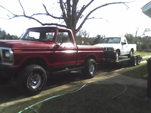 1979 Ford F-150 - A red 1979 Ford F-150 is seen towing a white pickup truck on a trailer.