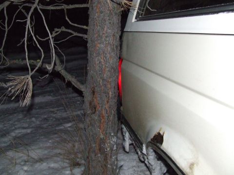 1990 Ford Bronco - A white SUV is stuck between trees in a snowy environment at night, with its rear taillight on.