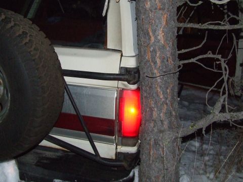 1990 Ford Bronco - The rear of a white SUV is visible, with a spare tire on the left and a red taillight glowing.