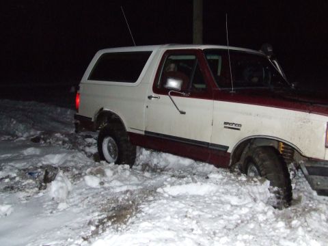 1990 Ford Bronco - The Ford Bronco is stuck in a snowy area at night, with its tires sunk deep into the snow.