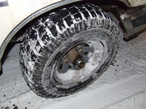 1990 Ford Bronco - A vehicle's tire and wheel are partially covered in snow, suggesting it has been driven in winter conditions.