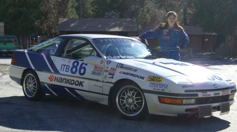 1990 Ford Probe - A woman in a racing suit stands next to a heavily stickered race car with the number 86.