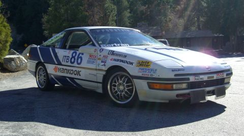 1990 Ford Probe - A white 1990 Ford Probe race car, adorned with blue racing stripes and sponsor decals, is parked outdoors.