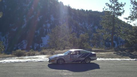1990 Ford Probe - A 1990 Ford Probe race car is seen parked on a roadside with a snowy mountain in the background.